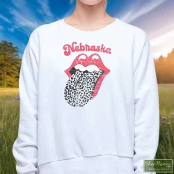 Leopard Tongue Rolling Stones Style Nebraska Huskers Shirt White 2 Women's Leopard Tongue Rolling Stones Style Nebraska Huskers White Sweatshirt In White, Front View On Dark Wood Background